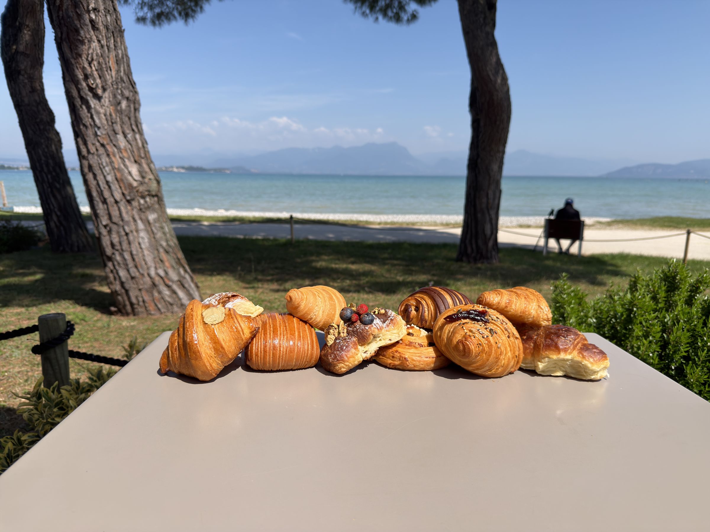 Brioche appena sfornate su un tavolo in giardino, con il lago di Garda e i pini sullo sfondo