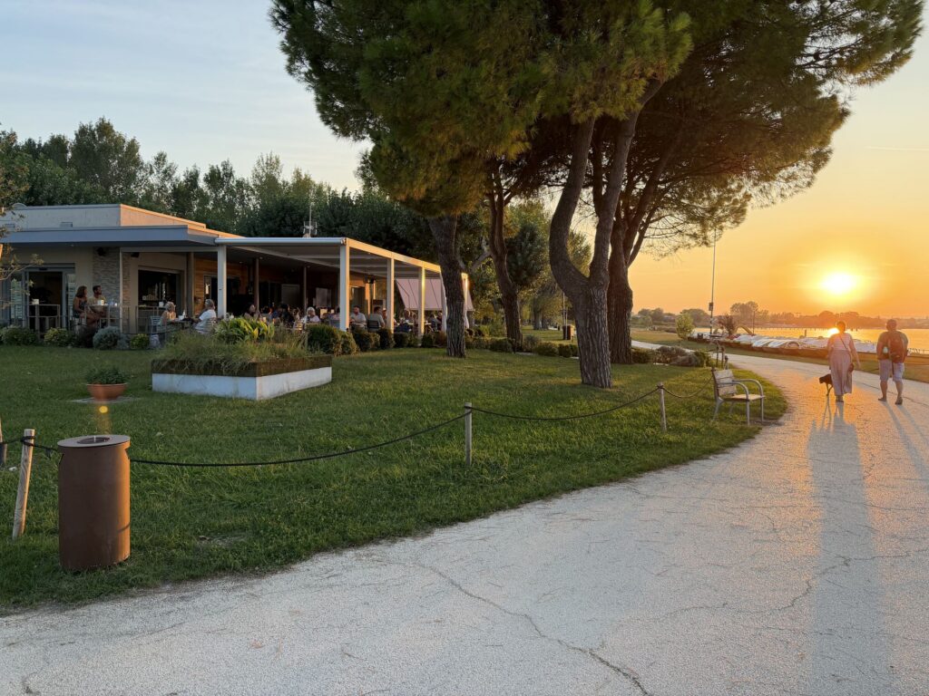 Il Punta Grò Bistrot e il giardino con il sole che tramonta tra i pini sul lago